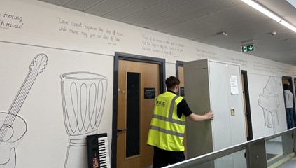 A BMG employee moving a cabinet down a school corridor