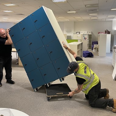 Two men loading a blue cabinet onto a small wheeled trolley