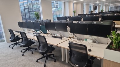 An open plan office with rows of desks, chairs and computer monitors